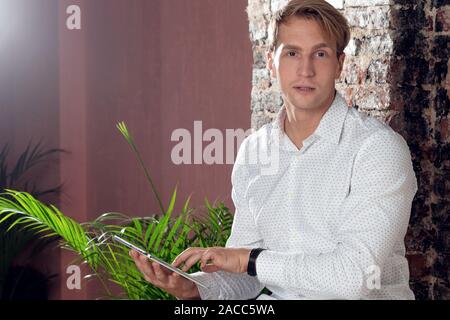 Porträt eines positiven und selbstbewussten jungen Mannes in einem klassischen weißen Hemd. Fröhlicher Kerlstudent mit dem Laptop, Porträt im Innenraum. Stockfoto