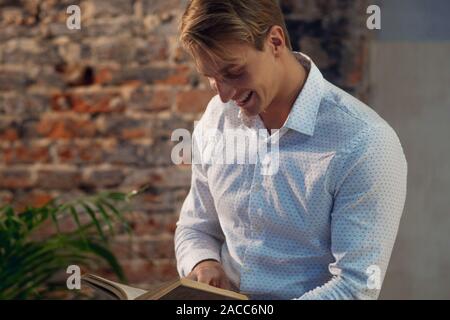 Eine junge lächelnde Mann in einem weißen Hemd, ein Buch zu lesen. Business Literatur zur Selbstentwicklung. Studenten oder junge Unternehmer. Stockfoto