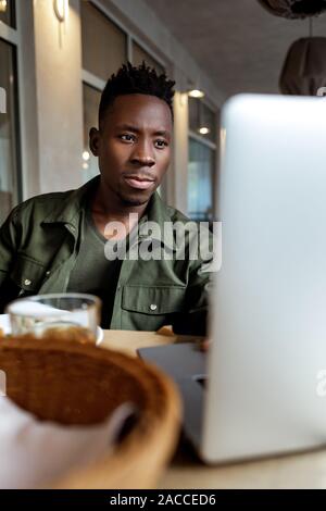 Junge afrikanische amerikanische Mann mit Laptop im Cafe Stockfoto