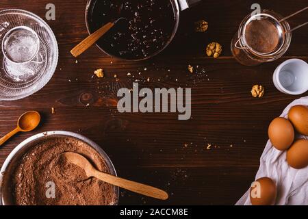 Schokolade Bäckerei Hintergrund. Zutaten für die brownies, Kakaopulver mit Mehl, Nüsse, Eier gemischt und Kochutensilien auf dunklen Holztisch, Stockfoto
