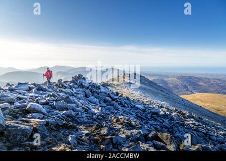 Eine einsame weibliche Wanderer und Walker im Winter, Wandern über den felsigen Grat auf der Oberseite der Elidir Fawr, ein Berg im Snowdonia National Park, Wales. Stockfoto