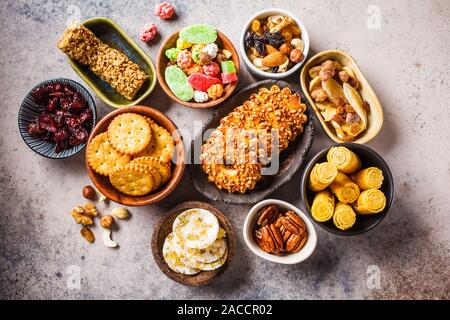 Auswahl an Snacks und Süßigkeiten auf grauem Hintergrund. Waffeln, Nüsse, Süßigkeiten, Kekse, Chips, Obst, Ansicht von oben. Stockfoto