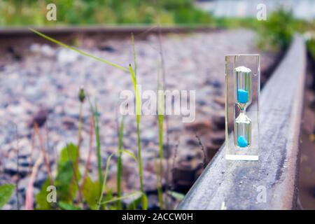 Transparente Sanduhr mit blauem Sand stehend auf dem alten rostigen Schiene, Konzept Stockfoto