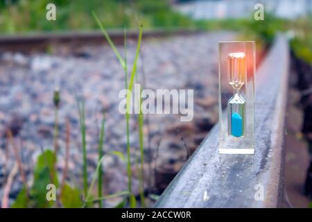 Transparente Sanduhr mit blauem Sand stehend auf dem alten rostigen Schiene mit Lichteffekt, Konzept Stockfoto