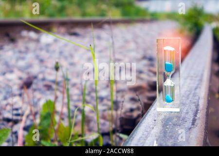 Transparente Sanduhr mit blauem Sand stehend auf dem alten rostigen Schiene mit Lichteffekt, Konzept Stockfoto