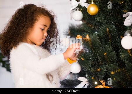 Afrikanische Mädchen schmücken Weihnachtsbaum zu Hause konzentriert Stockfoto