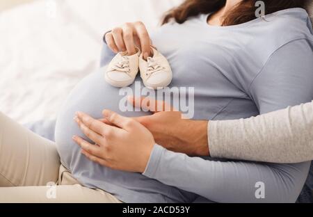Kleine Schuhe für das ungeborene Baby auf schwangeren Bauch Stockfoto