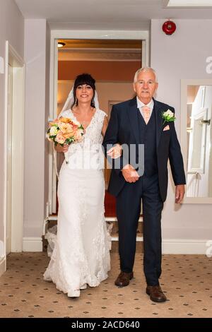 Ein stolzer Vater begleitet seine Tochter auf der insel, bereit für eine traditionelle englische Hochzeit im Manor in Cheadle, Stoke on Trent, Staffordshire Stockfoto