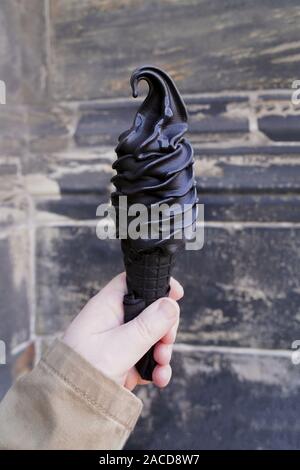 Hand hält schwarzen Softserve Eis-Konus mit gemacht Aktivkohle Stockfoto