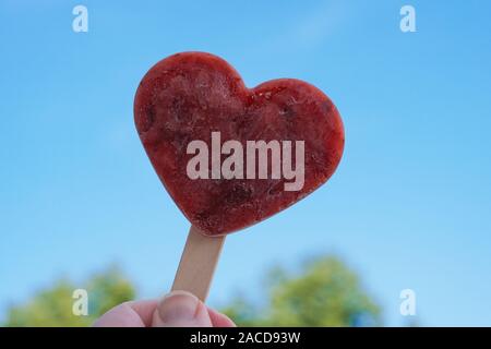 Hand, die herzförmige Hausgemachte berry Popsicle oder Eis am Stiel gegen den klaren blauen Himmel - liebe Sommer Konzept Stockfoto