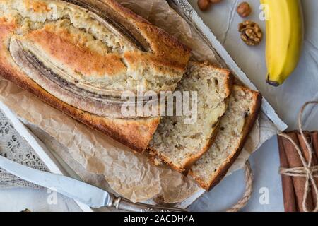 Frische hausgemachte Banana Bread in weißem Holz- Fach mit Zutaten aus Leichtbeton Hintergrund. Ansicht von oben. Stockfoto