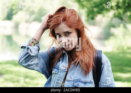 Junge Frau trägt Jeansjacke spielt mit ihren Haaren und einem coy schauen - authentische Menschen im Freien Stockfoto