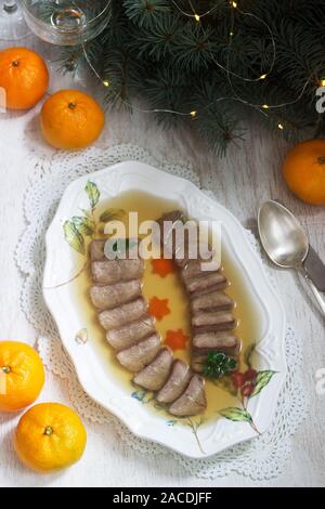 Aspic der Zunge verziert mit gekochten Karotten und Petersilie auf einem festlichen Hintergrund. Rustikaler Stil. Stockfoto