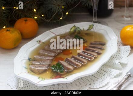 Aspic der Zunge verziert mit gekochten Karotten und Petersilie auf einem festlichen Hintergrund. Rustikaler Stil. Stockfoto