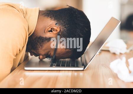 Überarbeitet Geschäftsmann mit dem Kopf nach unten auf dem Computer Stockfoto