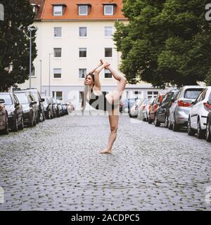 Unbeschwerte junge Frau Ballet Dancer Ausübung auf Straße der Stadt - städtische Ballerina tragen leotard zeigt Flexibilität und Lebendigkeit in Yoga pose Stockfoto