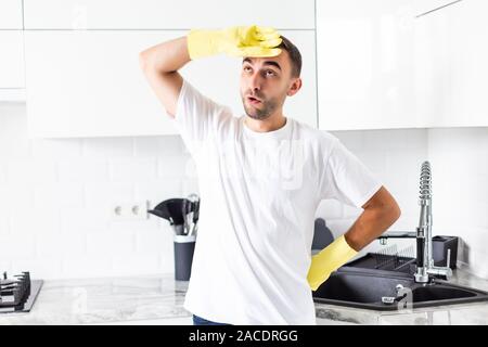 Junger Mann in Handschuhe für die Reinigung der Küche zu Hause bereit müde Stockfoto