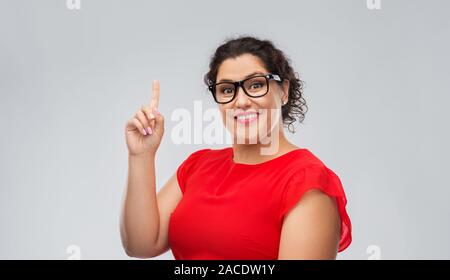 Glückliche Frau in Gläsern zeigt mit dem Finger auf Stockfoto