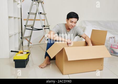 Hübscher junger asiatischer Mann auspacken Werkzeuge in der neuen Wohnung wird er umzubauen Stockfoto