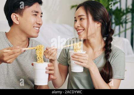 Studenten essen Instant Nudelsuppe aus Plastikbecher mit Stäbchen und bei jedem anderen Suchen Stockfoto