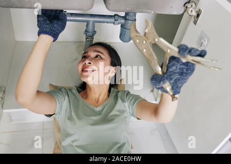 Fröhliche junge Frau Schutzhandschuhe bei der Festsetzung tropfende Spüle Rohr in der Küche Stockfoto