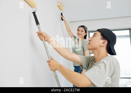 Hübsche junge lächelnde Haus Maler im Haus arbeiten mit ihren männlichen Kollegen und Kamera Stockfoto