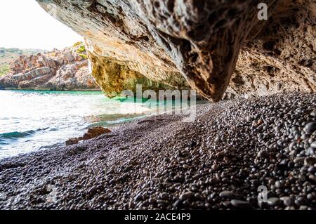 Erstaunlich seascape Blick von einzigartigen Meer Höhle über Wasser überhängenden am berühmten Strand von Cala Bianca malerische Umgebung. Kristallklare Meer Wasser Wellen waschen Stockfoto