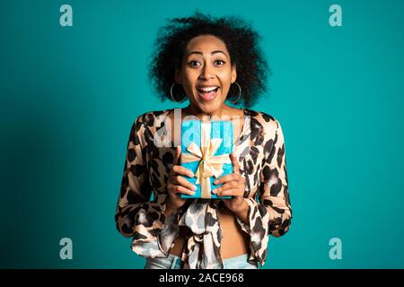 Schöne afrikanische amerikanische Frau empfing Geschenkbox mit Schleife. Sie ist glücklich und durch Aufmerksamkeit geschmeichelt. Mädchen in Studio Hintergrund. Stockfoto