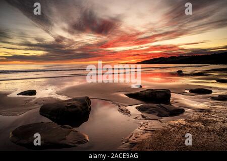 Charmouth, Dorset, Großbritannien. 2. Dezember 2019. UK Wetter: spektakuläre Farben werden im nassen Sand bei Ebbe wider, wie die Sonne über den Strand setzt bei der Küstenstadt Charmouth. Der beliebte Strand ist fast menschenleer, als die Sonne unter dem Horizont in Richtung Lyme Regis. Credit: Celia McMahon/Alamy Leben Nachrichten. Stockfoto