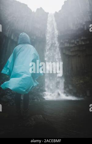 Frau in blauem Regenmantel bei Wasserfall in Skaftafell, Island Stockfoto