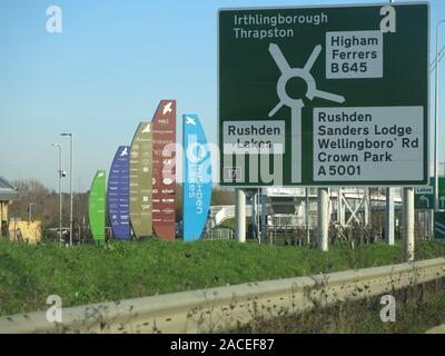 Der Ansatz entlang der A 45 in Richtung Osten am Kreisverkehr für Rushden Seen, mit Anweisungen für das Einkaufszentrum und Werbeflächen für die Geschäfte. Stockfoto