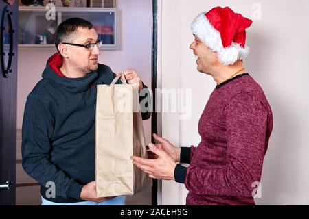 Reifer Mann hatte zu seinem Freund oder Verwandten mit anwesend, um Weihnachten zu feiern. Zwei Männer sind die Vorbereitung für das Neue Jahr, eine von ihnen trägt Santa's Hut. Stockfoto