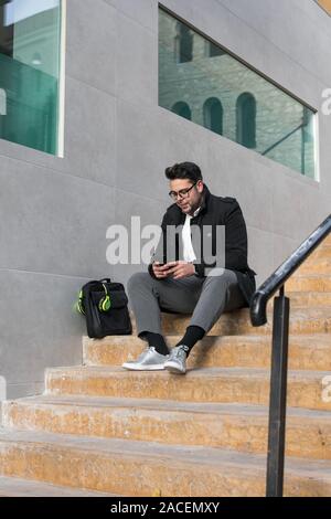 Foto von einem jungen Mann, während er sein Smartphone ist gerade auf der Straße Stockfoto