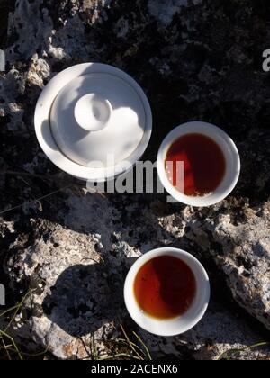 Reisen Konzept. Die schwarzen Tee in Weiß Chinesische gaiwan und Tassen auf Big Rock Top View kopieren Raum Stockfoto