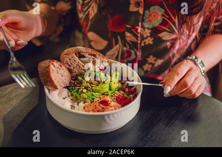 Frau essen Bio-lebensmittel. Frische Meeresfrüchte Rezept. Frischer Lachs poke Schüssel mit Reis, Eier, Brot, frischem Rotkohl, Avocado, Rettich Rosenkohl auf dunklen zurück Stockfoto