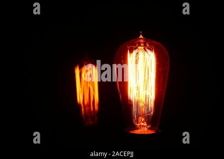 Klares Glas elektrische Glühbirne abgedunkelt, damit es den Tungsten Filament mit Reflexion gesehen werden Stockfoto