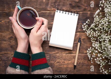 Frau trinkt ein heißer Kaffee aus einer Tasse und schreibt einen Text in eine leere Seite Notizblock mit Kopie Raum über holztisch Flachbild Hintergrund legen. Stockfoto