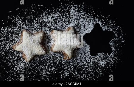 Frische Kekse in Form von Sternen mit weißer Zuckerglasur und Puderzucker gegen einen dunklen Hintergrund und Raum für eine fehlende Keks Stockfoto