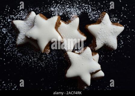 Frische Kekse in Form von Sternen mit weißem Zuckerguss und Puderzucker gegen den dunklen Hintergrund Stockfoto