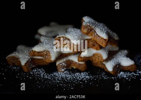 Frische Kekse in Form von Sternen mit weißem Zuckerguss und Puderzucker gegen den dunklen Hintergrund Stockfoto