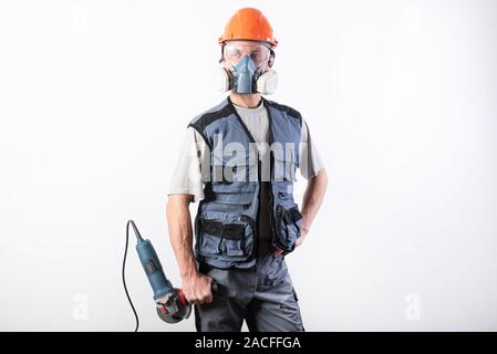 Builder in einen Helm und eine Atemschutzmaske, mit einem Winkelschleifer in seinen Händen. Stockfoto