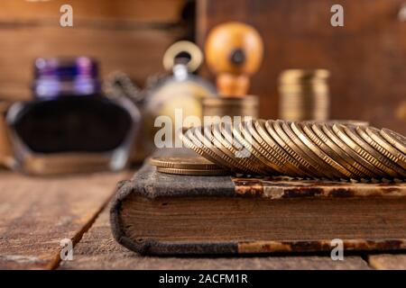 Münzen in Bars auf einem alten Buch angeordnet. Arbeitsplatz ein Buchhalter in einem alten Unternehmen. Der dunkle Hintergrund. Stockfoto