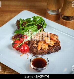 Reisgericht mit Fleisch auf dem Teller hinzufügen mit Garnelen, Tomaten und Salat. Grillen von Steak Stockfoto