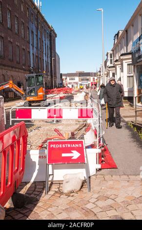 Straßenarbeiten den Bau einer neuen Straße Layout. Sicherheitsbarrieren und temporären Fußgängerzone Wanderweg in Position. Mann mit Stock Fußweg entlang zu laufen. Stockfoto