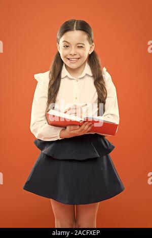 Schulmädchen Notizen auf orange Hintergrund. kleine Mädchen in Schuluniform. Schulmädchen holding Lektion buchen. Angaben form Buch. zurück zu Schule. nettes Mädchen halten Sie Notepad oder Tagebuch. Tagebuch für Mädchen. Stockfoto