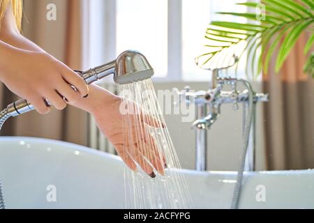 Wasser aus der Dusche auf die Hände des Mädchens. Auf einem blauen Hintergrund. Frau prüft die Temperatur des Wassers im Hintergrund der Badezimmer Stockfoto