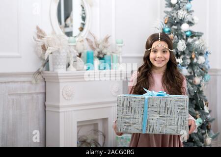 Weihnachtsgeschenk. Kleine Mädchen, das empfangene Geschenk. Beste Weihnachten Geschenke. Kind aufgeregt über ihr Geschenk. Kleine Mädchen in eleganten Kleid und Gift box christmas tree Hintergrund. Familie Traditionen. Stockfoto