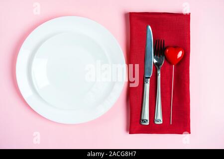 Festliche Tischdekoration für den Valentinstag mit Gabel, Messer und Herzen auf rosa Tabelle Hintergrund. Platz für Text. Ansicht von oben, flach. Stockfoto