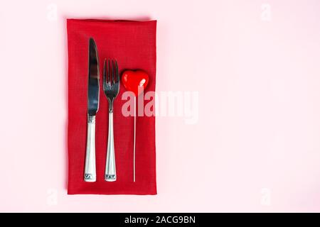Festliche Tischdekoration für den Valentinstag mit Gabel, Messer und Herzen auf rosa Tabelle Hintergrund. Platz für Text. Ansicht von oben, flach. Stockfoto