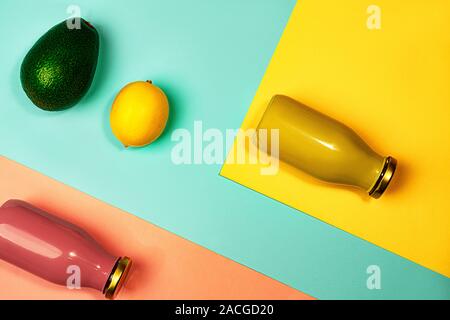 Flaschen bunte Säfte oder Smoothies, Zitronen und Avocados auf gelb, rosa Koralle und trendigen minze grün blau Hintergrund. Flach, Ansicht von oben, aus der Nähe. Minimalistischer Stil. Stockfoto